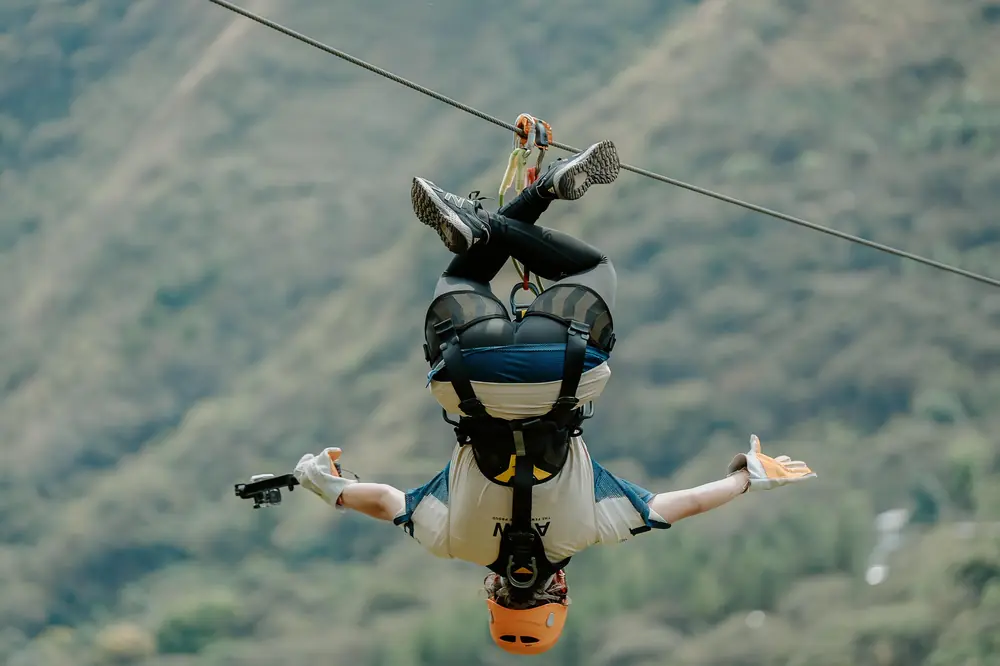 Rider going down the zipline upside down with arms out, filming with a camera